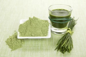 Green food supplements. Green juice, wheat grass powder and barley grass blades on green background. Detox and healthy living.