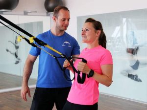 Trainer unterstützt Klientin beim TRX Schlingentraining – funktionelles Krafttraining mit Eigengewicht